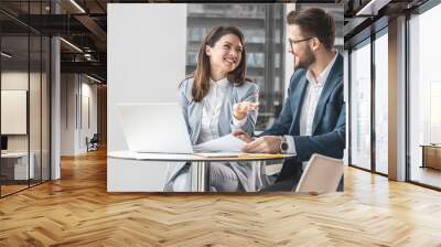 Two office workers discuss a new company project. They're sitting at the desk in the company cafe and preparing for a meeting.	 Wall mural