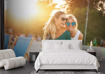 Two young female friends hangout at the  beach ,singing and relaxing in beautiful summer sunset.They hug each other.Best friends. Wall mural