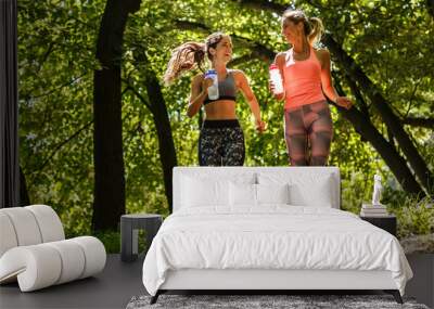 Two young female friends jogging at the woods.Laughing and making fun. Wall mural