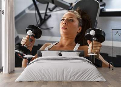 Woman lifting  weights and working on her biceps at the  gym Wall mural