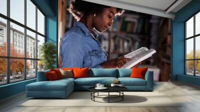 Young black female student reading a book in college library.	
 Wall mural