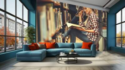 Young female student read and learns by the book shelf at the library.Reading a book.	
 Wall mural