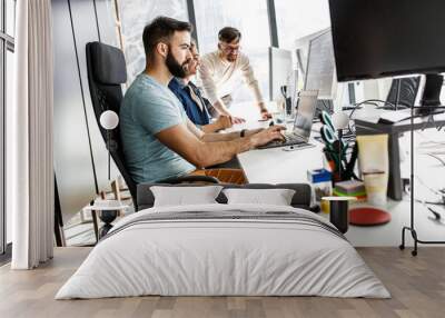 Young programmer sitting at the desk in his office and working .	
 Wall mural