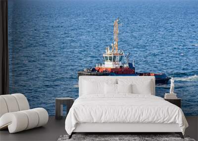 A tugboat navigates on the sea, in the background the coast can be seen  Wall mural