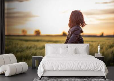 Back shot portrait of a young woman standing among long green grass in the field at sunset Wall mural