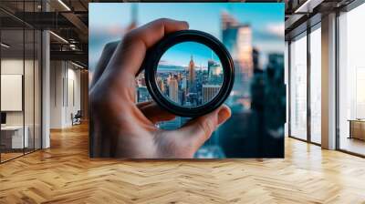 A hand holding a camera lens that is looking at a city. The city is New York and the lens is a viewfinder Wall mural