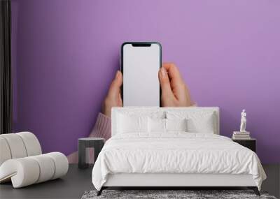 A person holding a phone with a white screen. The phone is on a purple background. The person is wearing a pink sweater Wall mural