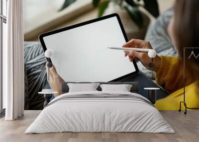 A woman is sitting on a couch holding a tablet and a pen. She is writing on the tablet. Mockup Wall mural