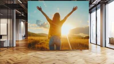 A woman is standing in a field with her arms raised, looking up at the sun. Concept of joy and freedom, as the woman seems to be celebrating the beauty of the moment Wall mural