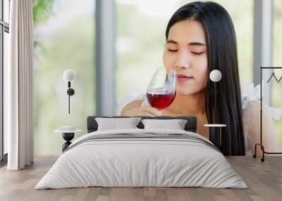 A beautiful young cute black long hair Asian woman sitting in a restaurant holding and smelling red wine in the glass Wall mural