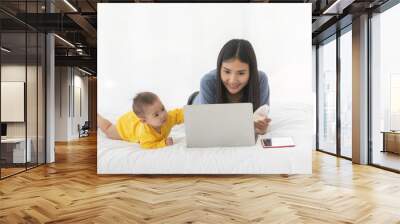 Adult asian woman mom smiling do feel happy and do speaking on smartphone and look at laptop with baby child on bed in the morning Wall mural