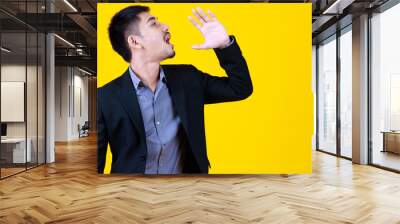 Asian business working beard handsome adult man wear formal suit, open large mouth, raise hand to announce, speak and shout out for advertisement, standing on isolated yellow background. Wall mural