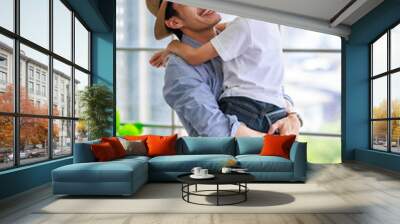 Asian happy cheerful joyful family young father wearing hat standing smiling bonding holding hugging cuddling lifting little preschooler boy son playing funny together in apartment home living room Wall mural