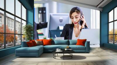 Asian young happy pretty female businesswoman employee staff in formal suit sitting smiling talking on smartphone call working consulting discussing with customer at working desk with laptop computer Wall mural