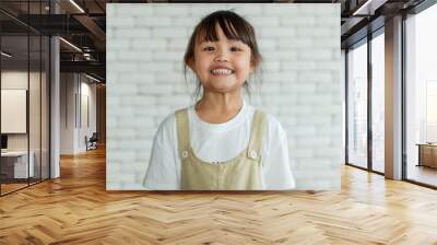 Close up portrait head shot of Asian long black ponytail hair young pretty girl  smiling wearing white shirt and brown bib apron standing alone in front of blurred white brick wall background Wall mural