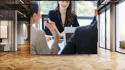 Closeup shot of Asian young happy beautiful professional successful businesswoman employee in formal business suit sitting smiling at working desk in company meeting room with blurred foreground Wall mural