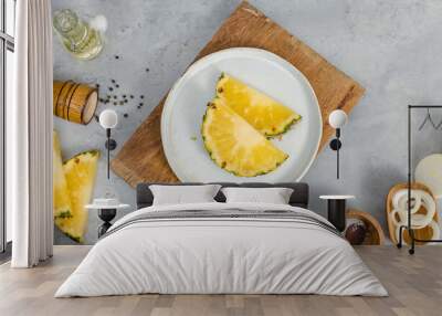 Closeup shot of two pieces sliced yellow pineapples on white dish on wood cutting board placed on table with other ingredients aroma oil in glass vial, pepper bottle, salt in wooden bowl and onion Wall mural