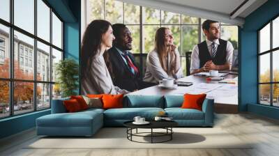 Group of four professional multiethnic businessmen and businesswomen sitting and concentrated listening to an idea of a new project in a multiracial organization meeting at the office working table Wall mural