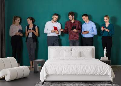 Group of six businesspeople colleague in modern company standing together in a row in front of the green wall and using smartphone. Wall mural