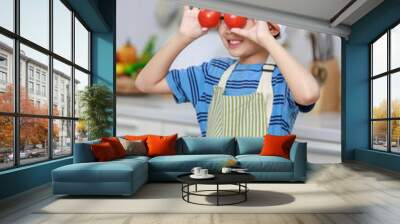 Millennial Asian little boy chef wearing tall white cook hat and apron standing holding red tomatoes cover eyes posing in home kitchen full of fruits vegetables and sliced bread on cooking counter Wall mural