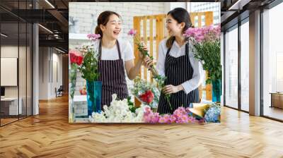 Millennial Asian young female flower shopkeeper decorator florist worker in apron smiling holding white flower bunch bouquet colleague use scissors cutting arranging decorating stalk in floral store Wall mural