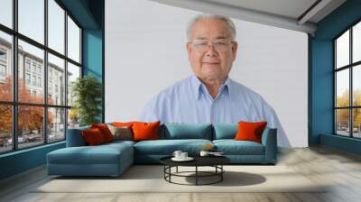 Portrait close up shot of asian old fat male model with short white and gray hair wearing eyeglasses and light blue shirt with stand smiling in front of white background Wall mural