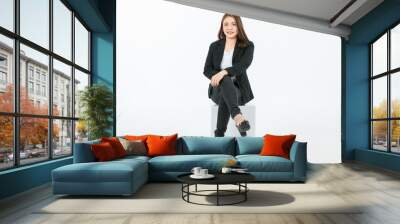 Portrait isolated cutout studio full body shot of Asian confident female professional successful businesswoman in formal black suit high heels sitting on square box look at camera on white background Wall mural