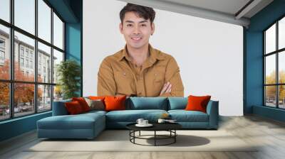 Portrait isolated cutout studio shot Asian young happy trendy male businessman model in casual brown long sleeve shirt with earring standing smiling holding hand in pants pocket on white background Wall mural