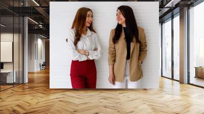 Portrait shot of two young Asian office workers in formal clothes standing, crossed arm and looking at each other and talking with a cute smiling on white background. Close friends and team concept. Wall mural