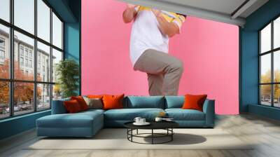 Portrait studio shot of Asian young handsome urban teenager fashion male model in street style outfit t shirt sport beige pants and red bucket hat standing posing look at camera on pink background Wall mural