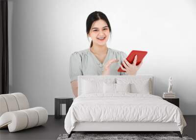 Studio shot of Asian young beautiful teenager female model with ponytail hairstyle wearing casual crop top outfit standing holding using touching touchscreen tablet in the red case on white background Wall mural