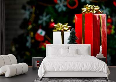 Studio shot of tall gift boxes with shiny golden ribbon placed on wooden table with colorful glossy bow tie in front decorative beautiful Christmas eve pine tree in blurred background Wall mural