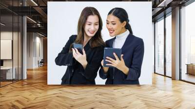 Studio shot of two Asian young beautiful female professional successful businesswoman model in formal business suit standing smiling holding tablet computer looking at smartphone on white background Wall mural