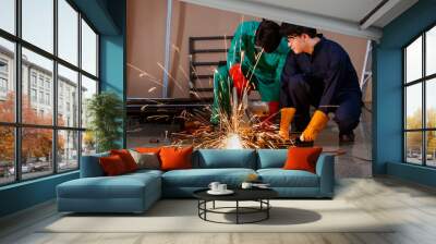 teamwork concept. Confident mechanic wearing safety outfit working carefully in a factory's workshop. They are using a steeling cutting machine to cut the metal rod and making a spark Wall mural