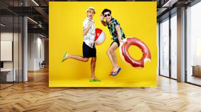 Young naughty guys in hot summer dresses acting funny jump with float ball and swimming tube as enjoy beach vacation with outdoor recreation game to play with happy friend Wall mural