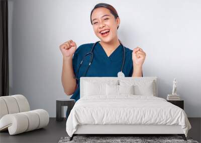 Excited Asian woman nurse wearing blue uniform with a stethoscope showing triumphing and celebrating victory, saying yes, achieving goal isolated on white background. Healthcare medicine concept Wall mural