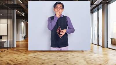 Portrait of shocked young Asian man wearing shirt and vest showing empty brown wallet isolated on white background Wall mural