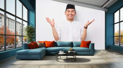 Smiling friendly handsome young Asian Muslim man wearing Arabic costume standing with wide raised arms and welcoming Ramadan isolated over white background. People religious Islamic lifestyle concept Wall mural