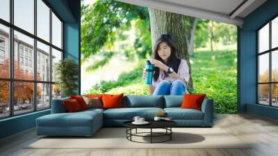 Asian woman drinking coffee while sitting in the park  Wall mural