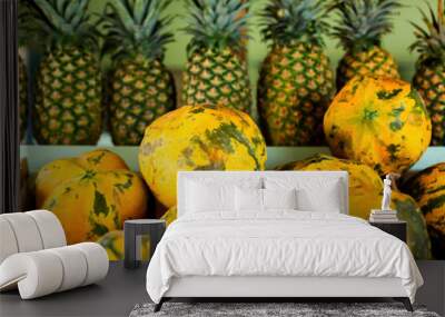 Ripe big fruits of juicy papaya and a row of pineapples on the background on the counter of a tropical country fruit shop Wall mural