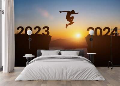 Happy new year 2024 concept. Silhouette of man jump on the cliff between 2023 to 2024 years over sunset or sunrise background. Wall mural