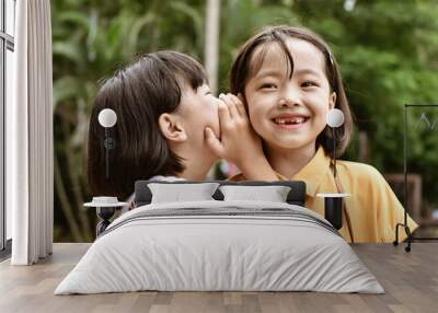 Two little sister girls whisper in ear at park outdoor. Wall mural