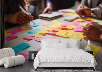 Diverse team collaboratively brainstorming with colorful sticky notes on a bright table in a creative office environment.
 Wall mural