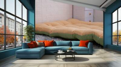 A side view of the orange and green extra mattress (Topper) neatly laid out on the floor in the middle of the bedroom. Wall mural