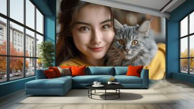 Young Asian Woman Holding Cute Grey British Shorthair Cat in Modern Living Room, Smiling and Playing with Fluffy Pet on Sofa, Happy and Adorable Pet Love at Home Wall mural