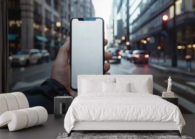 A person holding a smartphone with a blank screen in the foreground, with a bustling city street in the background. This image highlights modern technology amidst an urban environment Wall mural