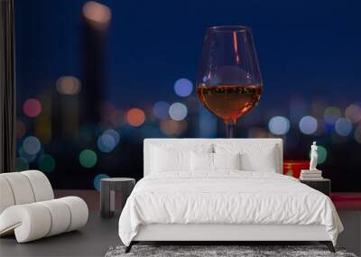 A glass of Rose wine with red candle on table and colorful city bokeh light background. Wall mural