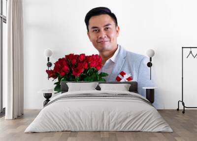 Asian man wearing grey suit holding a bouquet of red roses and red gift box isolated in white background for anniversary or Valentine's day concept. Wall mural