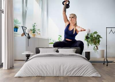 Athletic woman doing squats with kettlebell during home workout Wall mural