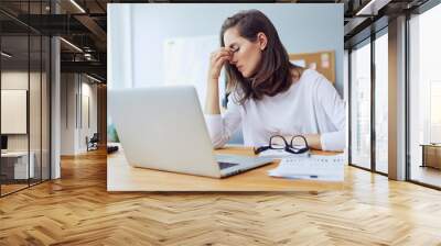 Beautiful stressed young office worker sitting at desk holding head because of pain in office Wall mural